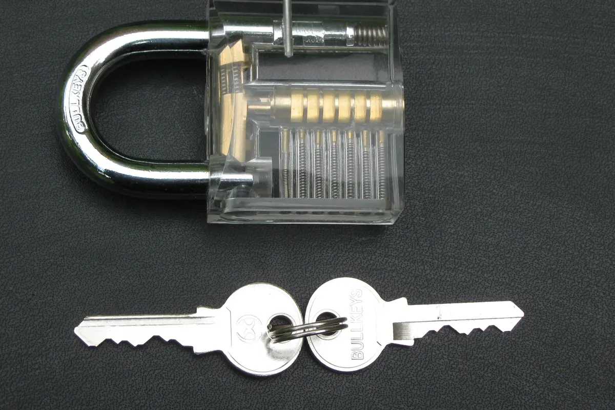 A transparent practice padlock beside two metal keys on a white surface.