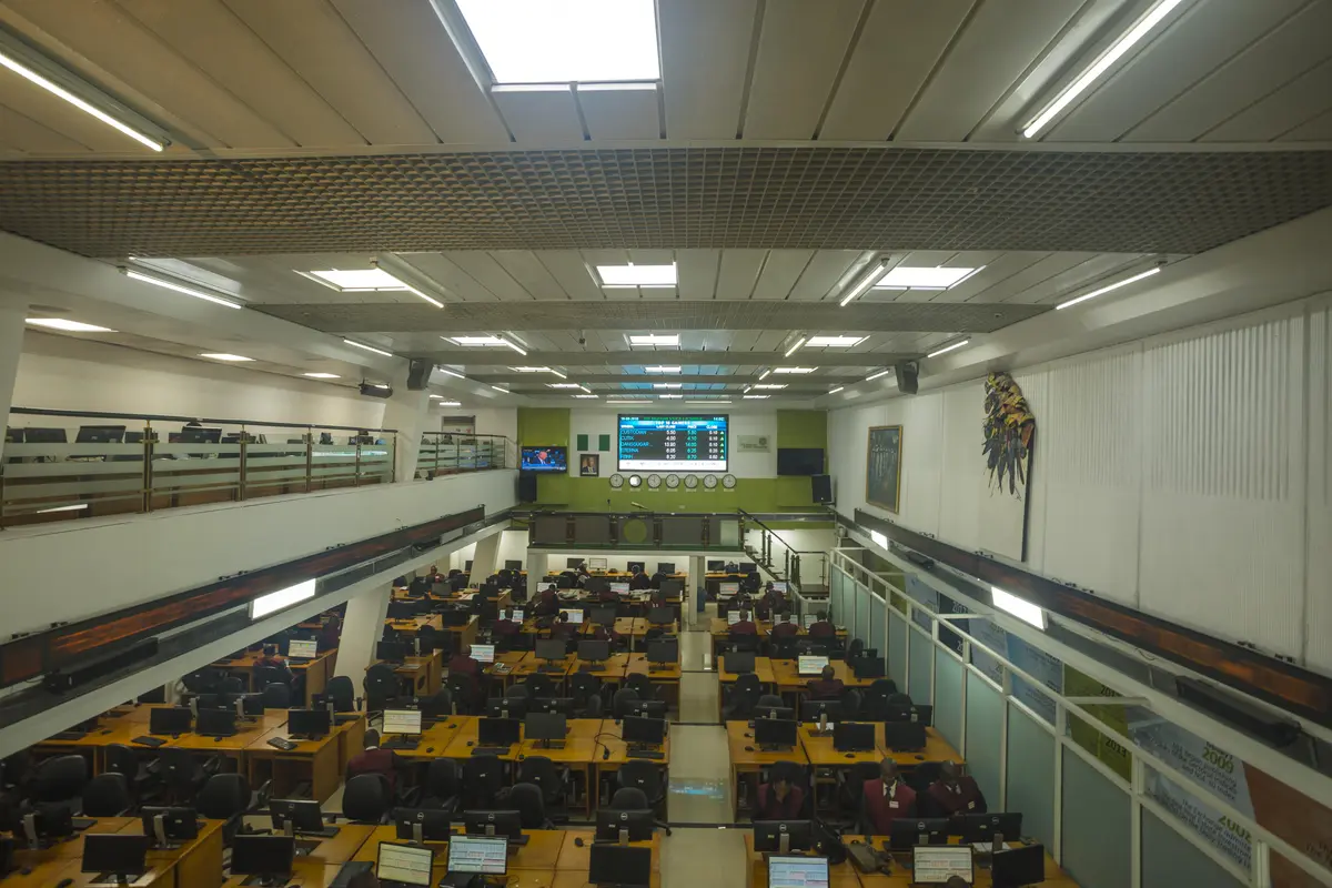 A wide view of a stock-exchange trading floor with desks, monitors and a price board.